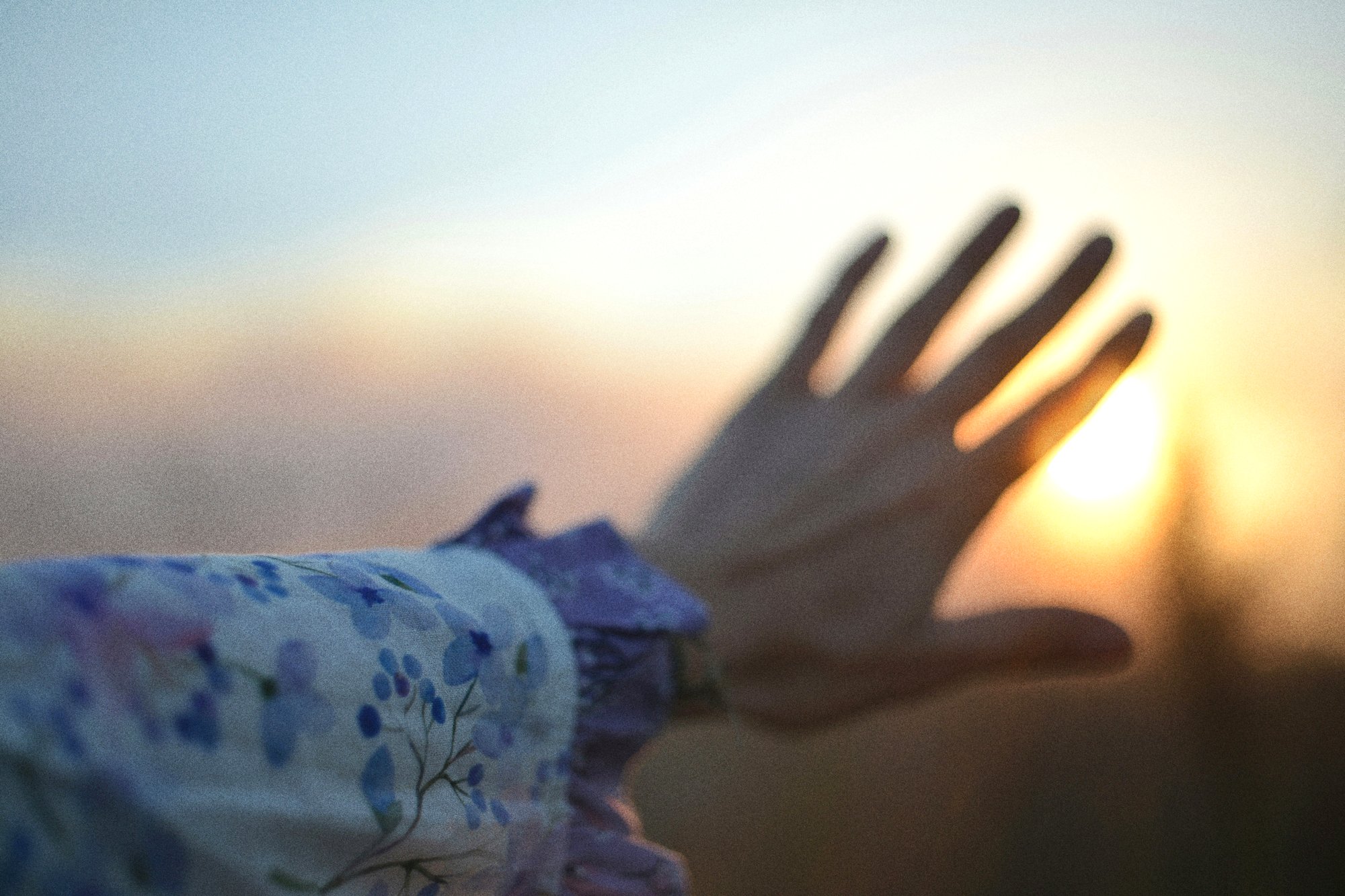Real film photograph: hand reaching toward sunset gold light