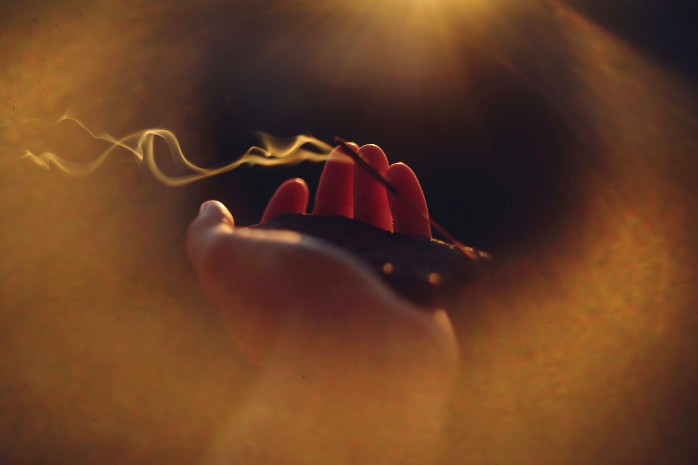 Real film photograph: hand holding incense with drifting smoke in warm gold light
